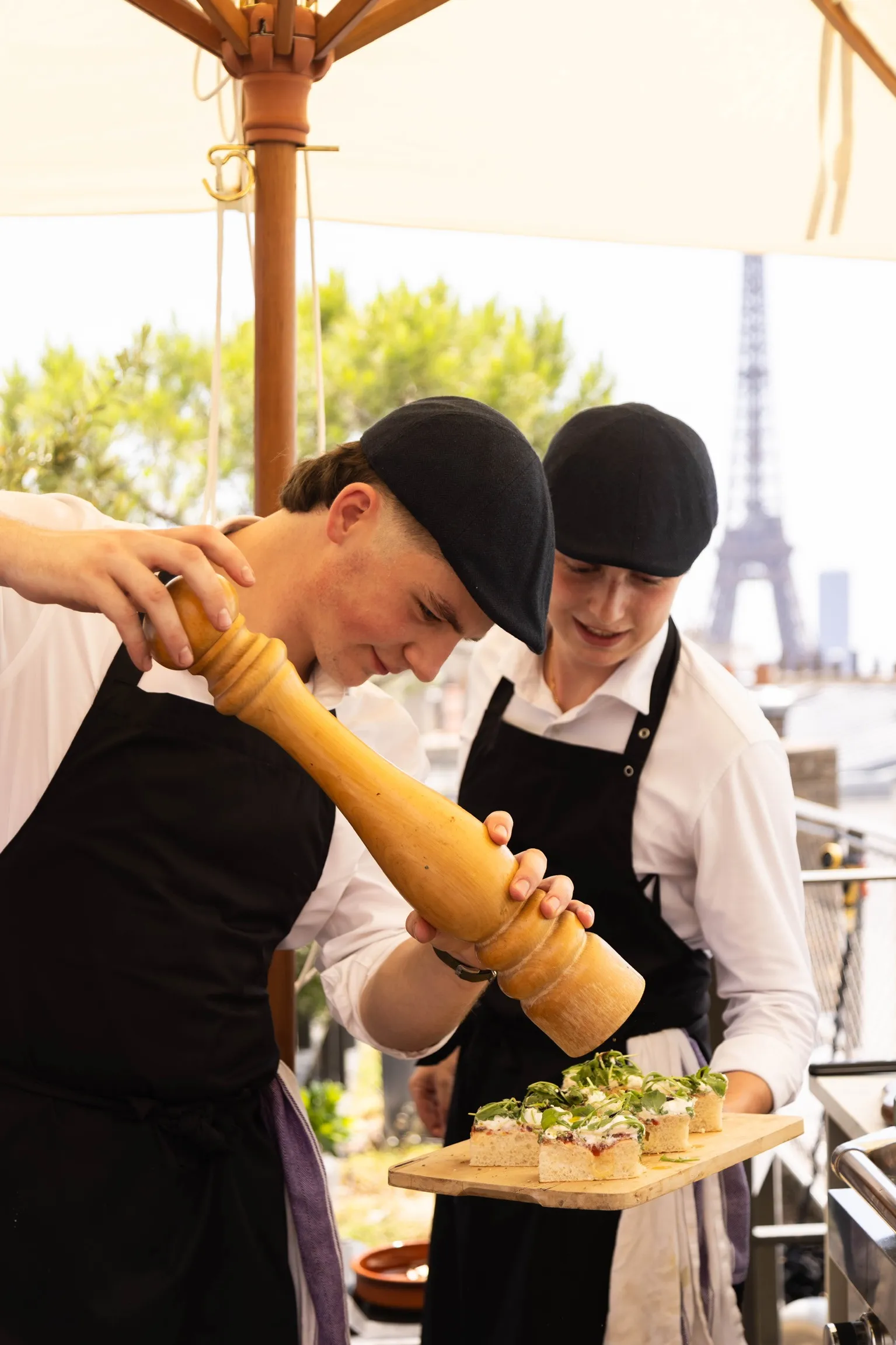 Aymeric et Raphaël, coiffés de leurs bérets, dressent des bouchées sur une terrasse face à la tour Eiffel